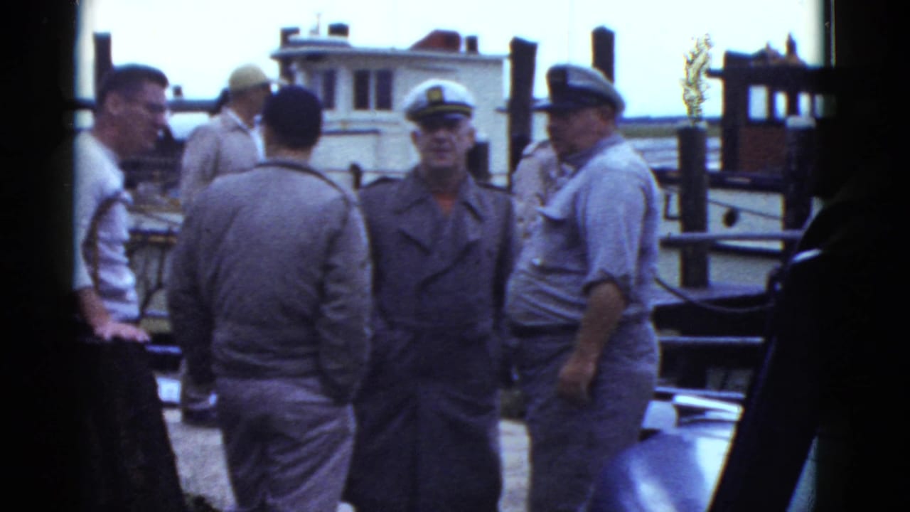 Group of adult men, including uniformed men in caps, standing by a docked boat.