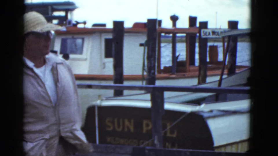 A man in a light cap appears at the edge of a 1951 Boston dock scene, with SUN PAL lettering, water, pilings, and boats behind him.