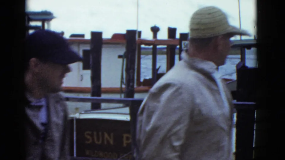 Two men in caps move through a Boston dock view from 1951 metadata, with the SUN PAL boat and SEA WOLF sign partly visible behind them.