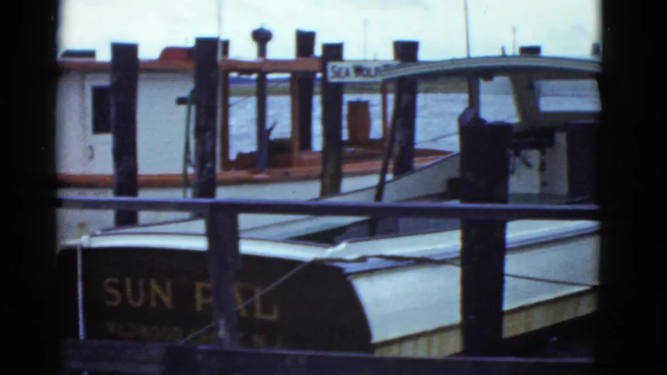 The camera holds on the docked cabin boat and wooden pier, with partial SUN PAL lettering visible in the lower frame.