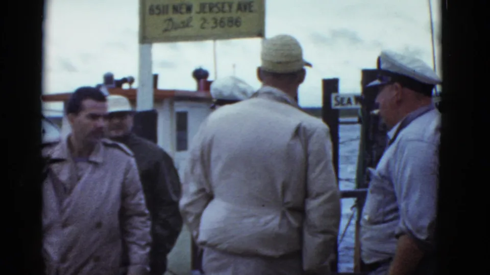 Boston 1951 frame of men on a waterfront dock, with a visible sign reading 6511 New Jersey Ave. and water behind the group.