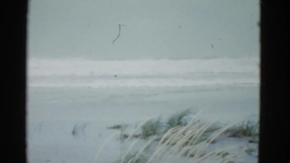 1951 Boston-area coastal view with muted surf, dune grass, and heavy dark borders from the 8mm frame or viewpoint.