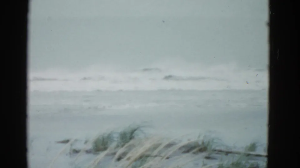 1951 Boston-area home-movie frame showing breakers offshore, dune grass below, and dark vertical edges around the view.
