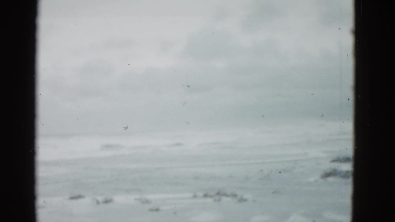 Soft 8mm frame showing a pale horizon or shoreline-like view before the street activity begins.