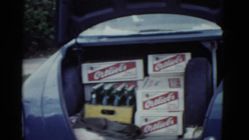 The open trunk of a mid-century car holds Ortlieb's beer boxes, a crate of bottles, and clothing or cloth items.