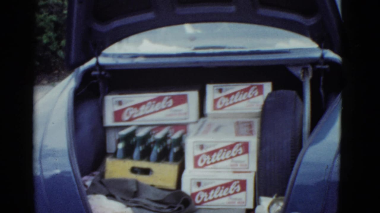 1951 Boston home-movie frame showing an open car trunk loaded with Ortlieb's beer boxes, a wooden bottle crate, glass bottles, cloth, and a spare tire.