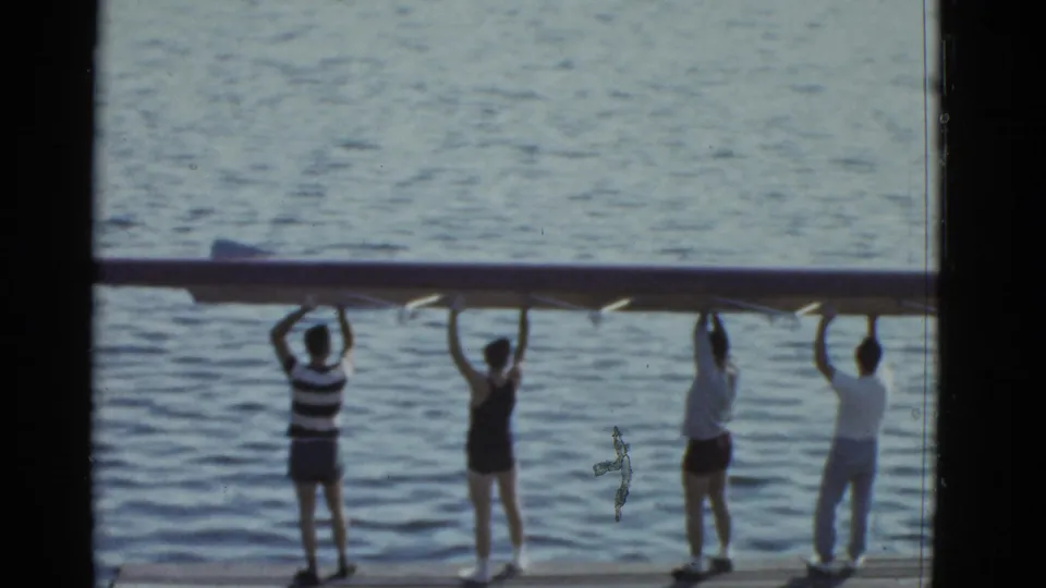 Final home-movie frame shows people along a waterfront carrying a long boat overhead, following the car-trunk packing sequence.
