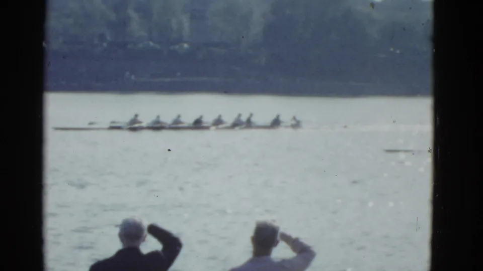 1951 Boston 8mm frame showing a long rowing shell near mid-frame with two spectators watching from the lower edge.