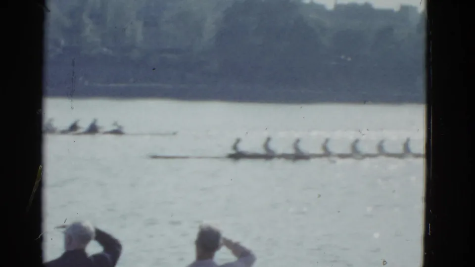 1951 Boston 8mm frame showing two crew shells on calm water as foreground spectators continue watching the race.