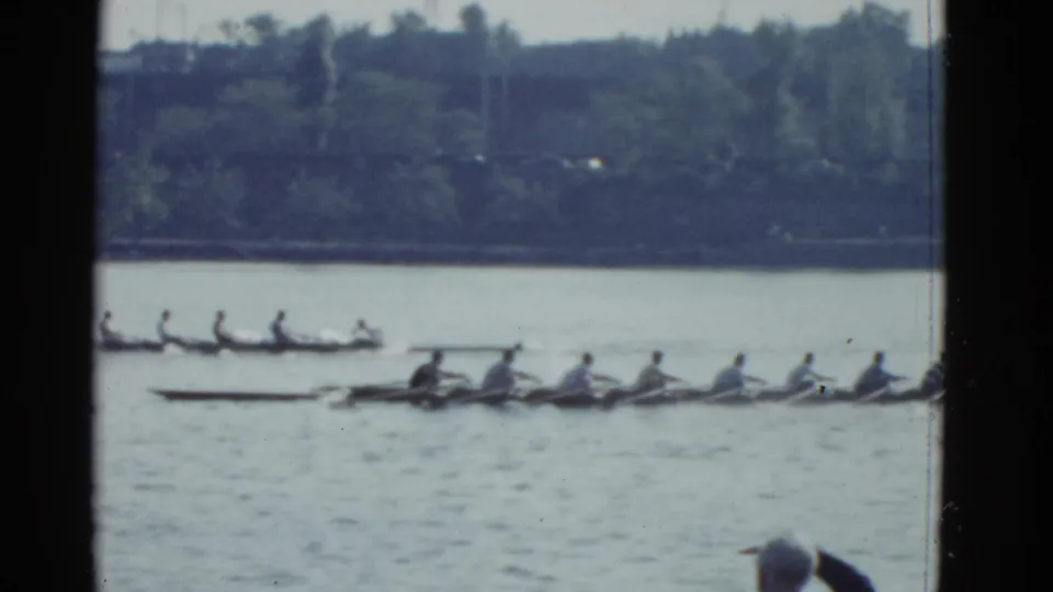 Multiple rowing crews move across the water in 1951 Boston footage, framed by dark 8mm film borders and a distant shoreline.