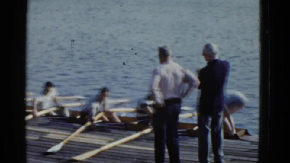 Two men stand on the dock watching rowers prepare in the shell, likely during a 1951 Boston rowing outing.