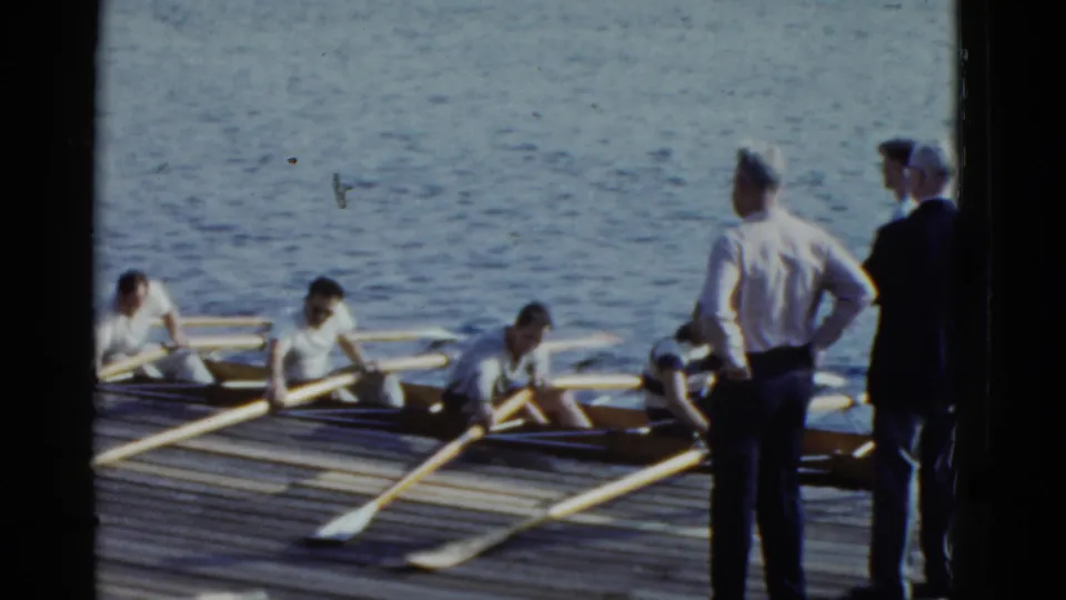 Boston rowing crew members handle their oars in a shell as standing men observe from the dock in 1951 home-movie footage.