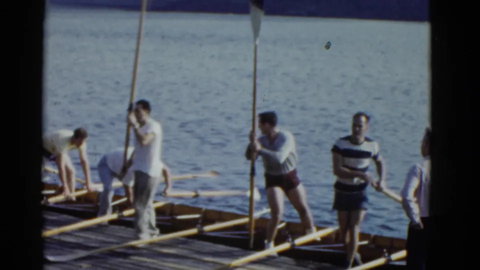 Boston 1951 home-movie frame showing rowers and a striped-shirt man standing among oars and shells on a waterfront pier.