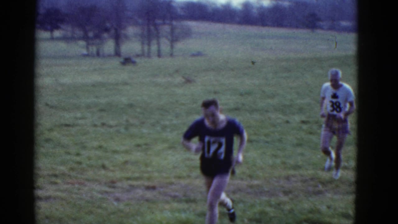 A runner in a dark numbered shirt leads another runner in a white numbered shirt.