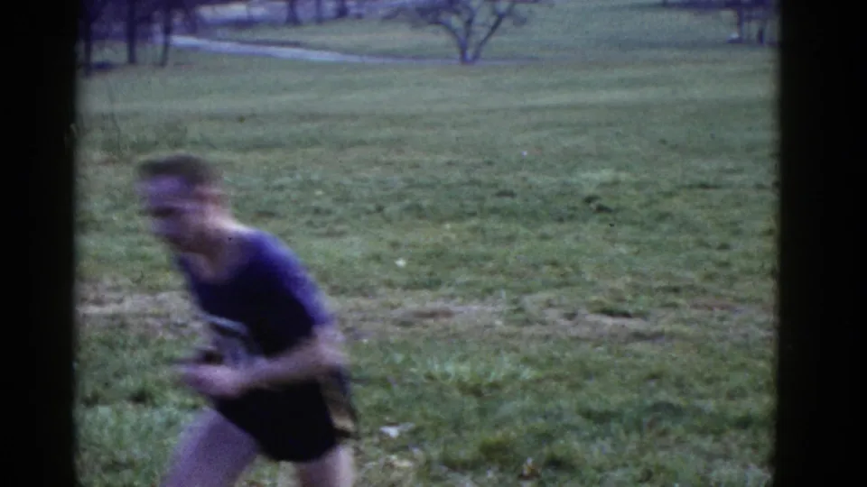 The lead runner moves past the camera at close range, blurred by handheld 8mm motion.