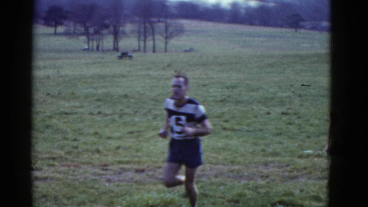 Male runner wearing bib number 5 moves across a grassy field.