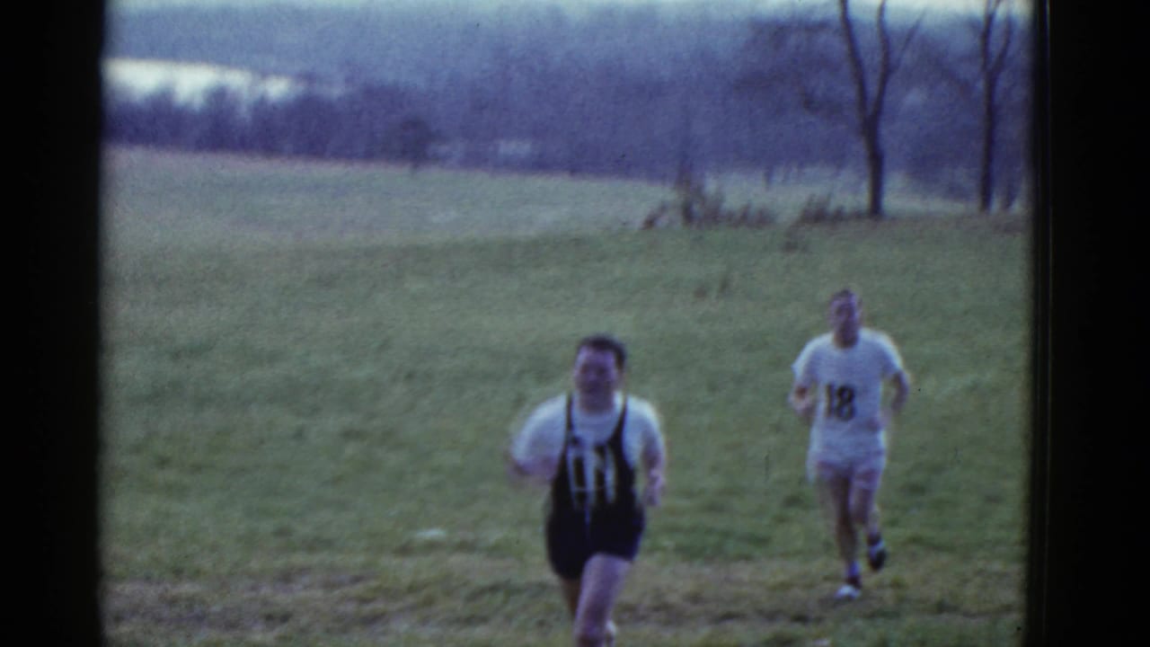 Runner in a dark number 11 singlet leads another runner wearing a light shirt with number 18.