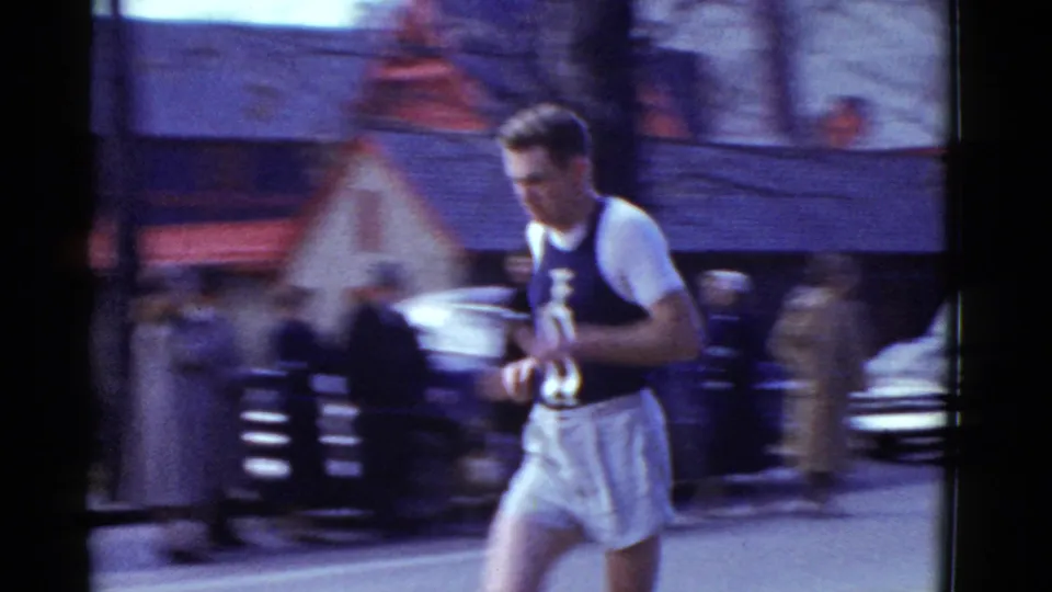 Close roadside view of a male runner in 1951 Boston, with motion blur, spectators, and parked cars in the background.