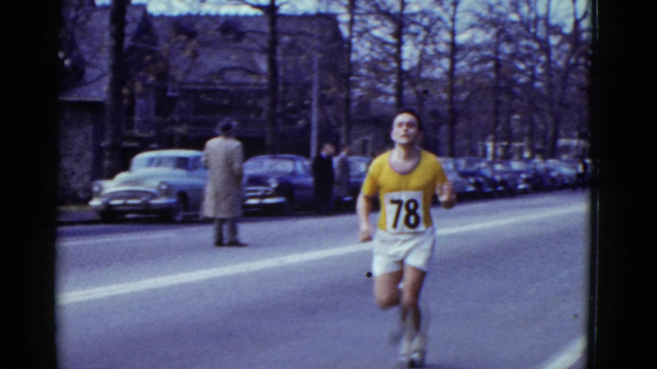 In 1951 Boston, a male runner wearing a yellow jersey and bib 78 runs past spectators and parked mid-century cars.
