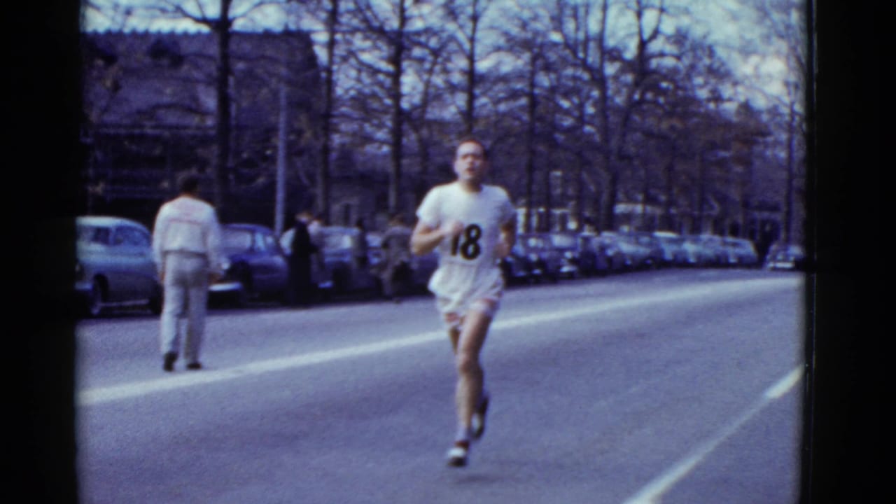 Runner wearing number 18 passes closer to the camera on a city street.