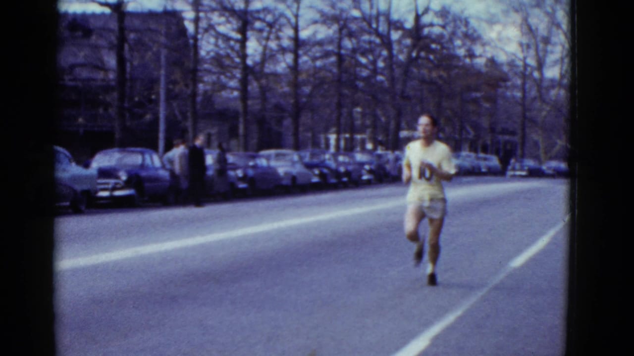 A different numbered runner appears to approach the camera on the same Boston street, with spectators and parked cars along the curb.