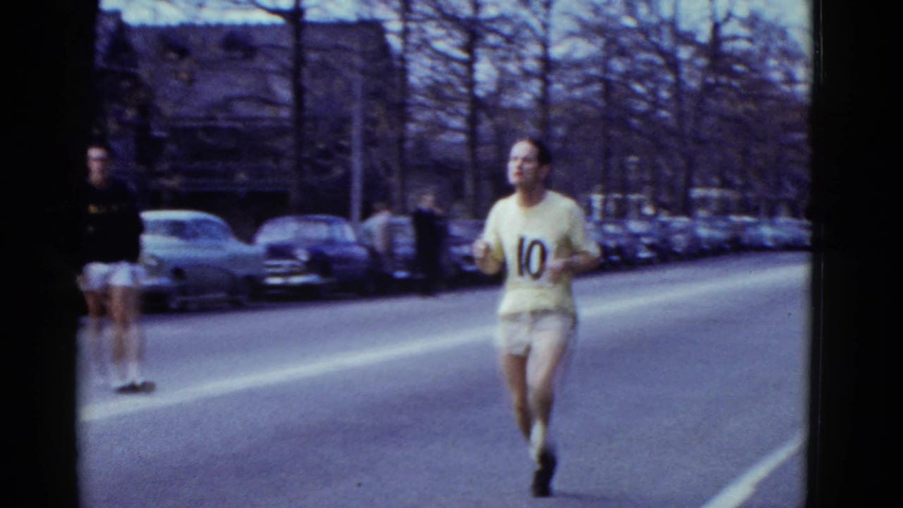Runner wearing number 10 moves along a street lined with parked cars and bare trees.