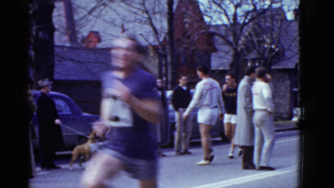 Runner blurs past spectators on a city street lined with parked cars.