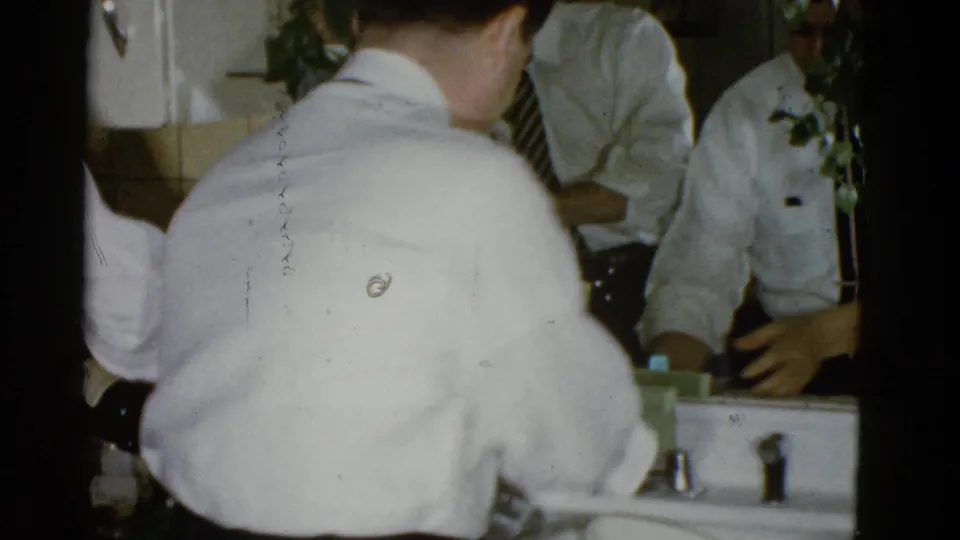 A 1951 Boston kitchen view shows a man from behind at the sink, with other adults reflected in the mirror above it.