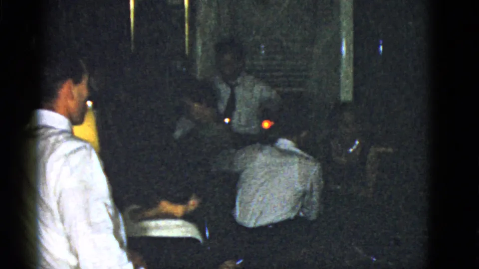 Several adult men appear seated and standing in a dim 1951 Boston private interior, partly hidden by shadow and film grain.