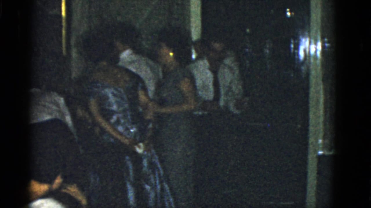 A low-light 1951 Boston party frame with a woman in a reflective dress beside men in light shirts and ties.