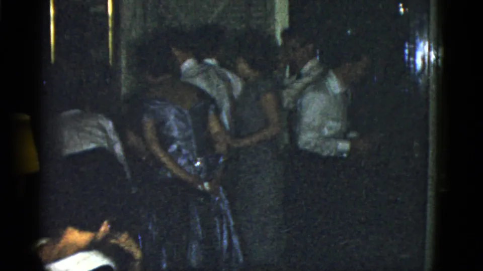 1951 Boston home-movie frame showing a crowded party group near a wall or doorway in low light.