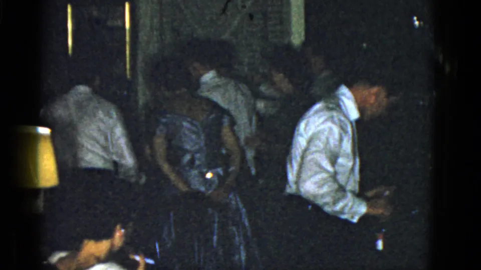 Low-light 1951 Boston home-movie frame showing party guests bending and moving through a crowded private interior.
