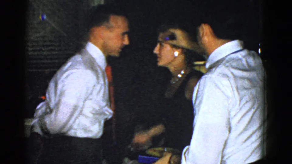 Two men in white shirts stand close to a woman wearing pearls, suggesting conversation or dancing during the 1951 Boston interior gathering.
