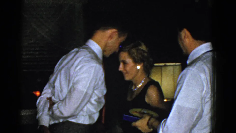 The woman appears to smile beside two men in white shirts, with a table lamp behind them in the 1951 Boston interior.