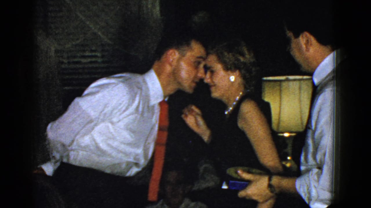 Man in a white shirt and red tie leans toward a smiling woman at an indoor party.