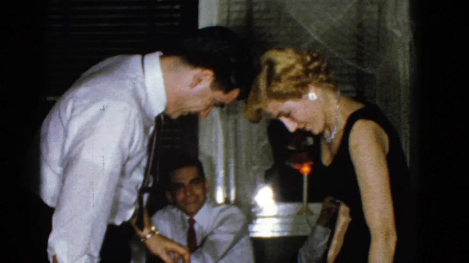 A man and woman lean forward in a Boston private interior, with another seated man briefly visible behind them.
