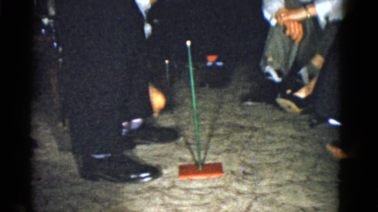 Coworkers stand and sit around a carpeted floor with a green stick on a red base.