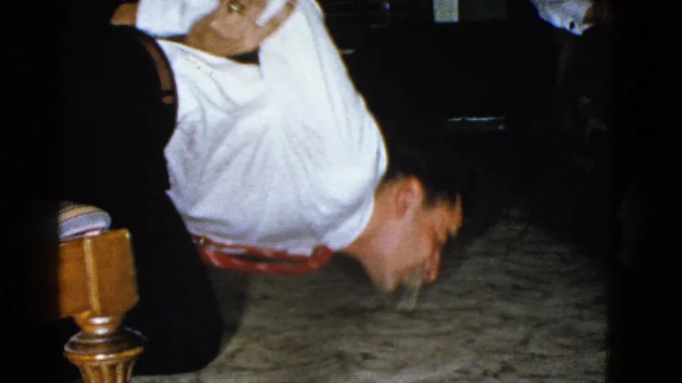 The 1951 Boston office-break footage shows a man in a white shirt and red belt upside down on the carpet while others watch nearby.