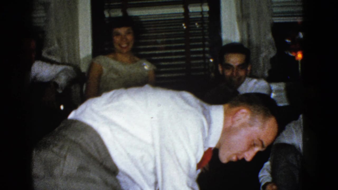 Man bends forward during charades while guests watch from the background.