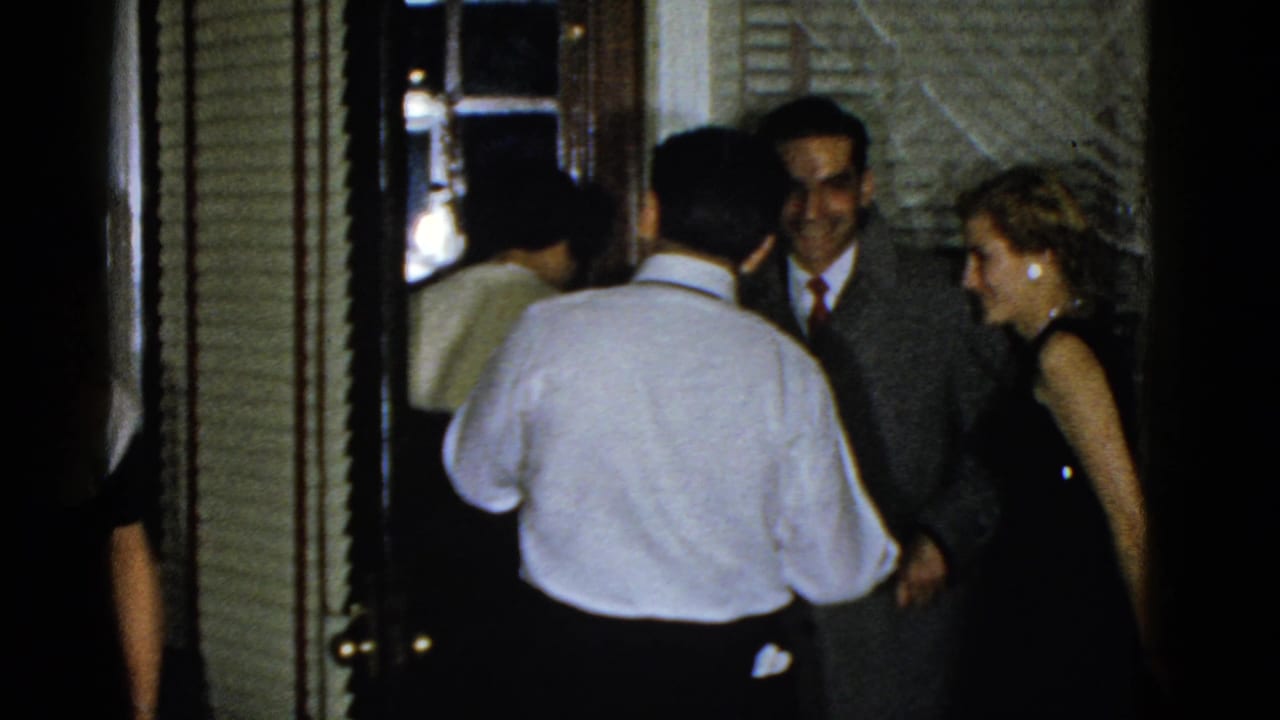 Adults stand near an open doorway while a man in a light shirt faces away.