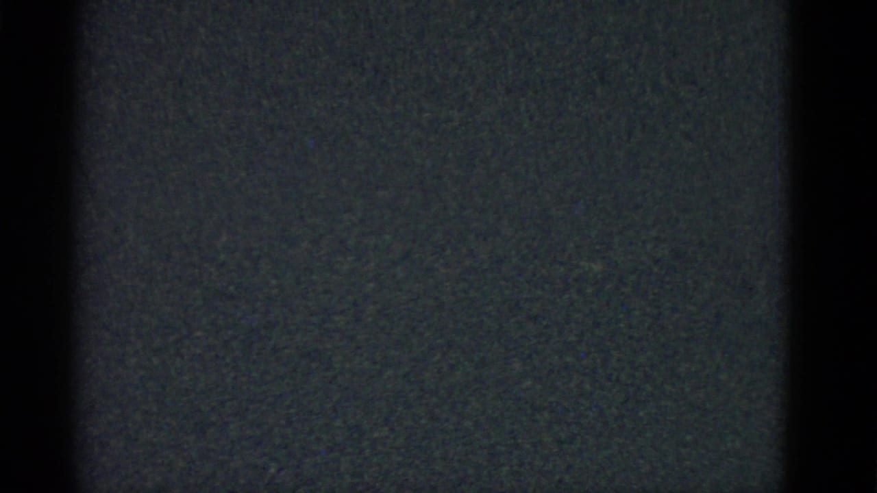 Nearly black 8mm frame with faint blue-gray grain and soft vertical edge darkness.