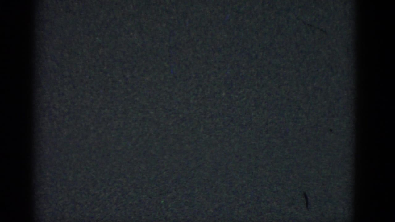 Dark 8mm frame with coarse grain, faint tonal banding, and small specks.