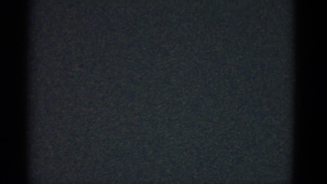 Underexposed 8mm frame showing grain and black film borders, likely a transitional moment before the domestic scene.