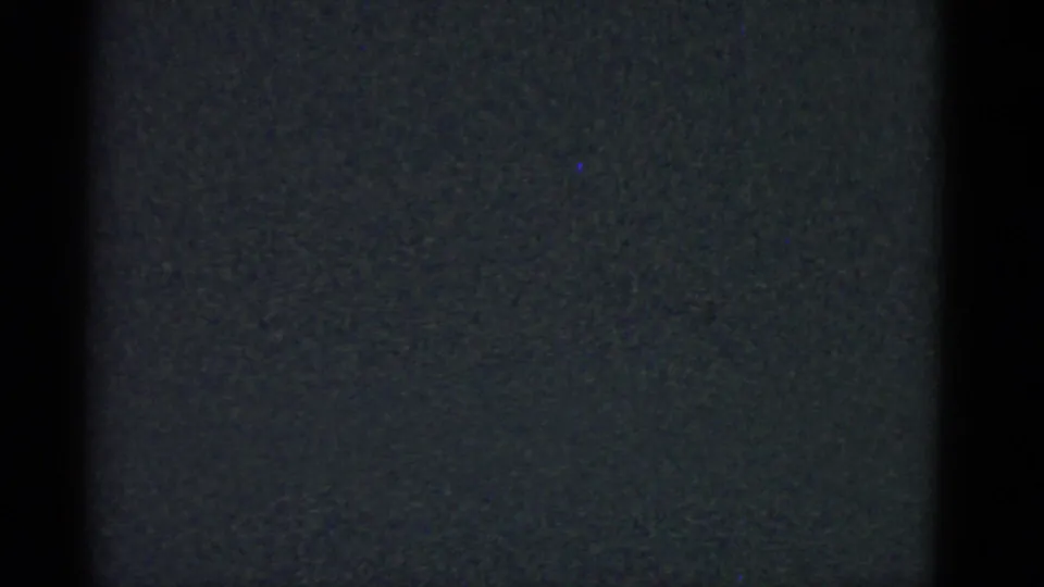 Mostly dark 8mm home-movie frame with faint texture and no clearly identifiable subject in view.