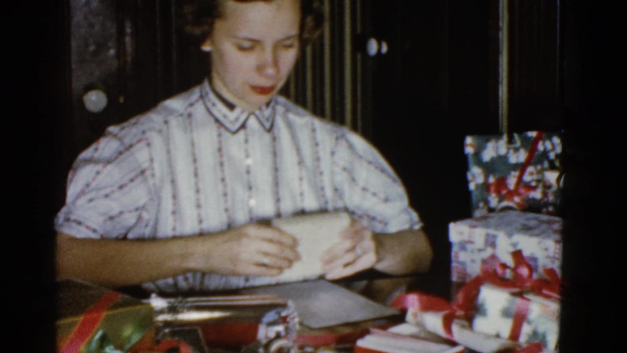 Woman seated at a table holding wrapping paper near ribboned gifts.