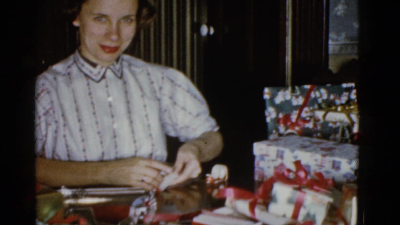 Young woman looks toward the camera while handling wrapping materials beside gift boxes.