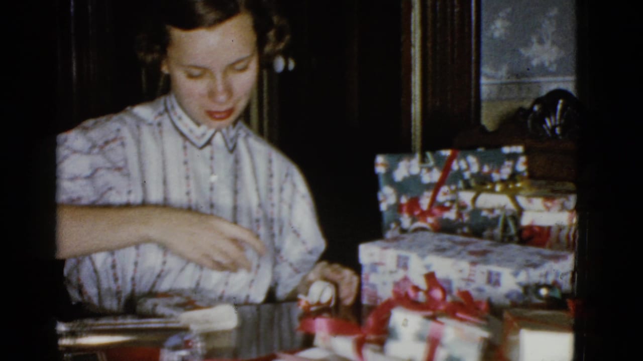 Young woman reaches across a table while wrapping presents with ribbon and paper.