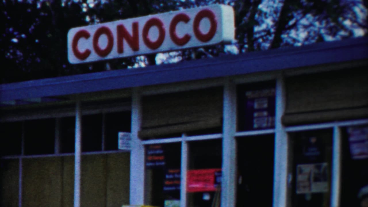 Conoco gas station storefront with roof sign, windows, and trees behind it.