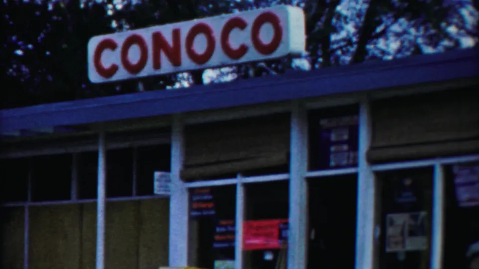 1958 Cheyenne County, Kansas view of a Conoco station exterior with red roof signage, white trim, glass windows, and trees in the background.