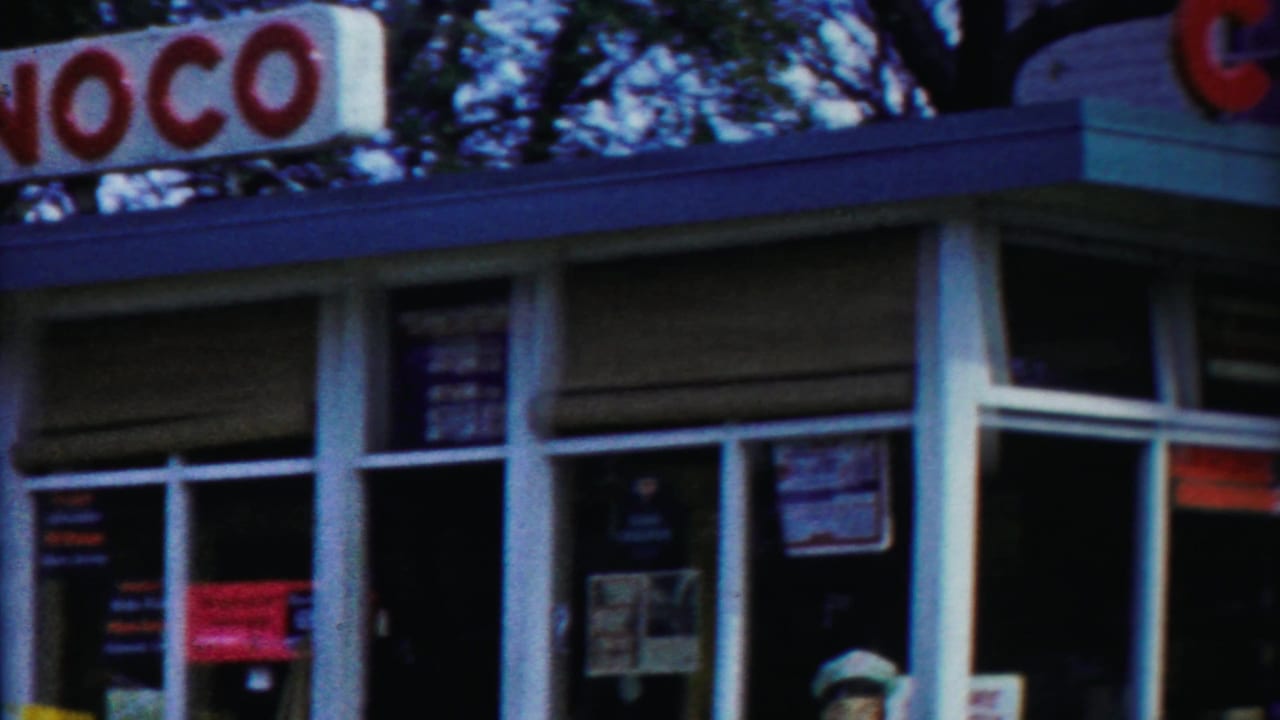 Conoco service-station frontage in Cheyenne County, Kansas, with red lettering, white-framed windows, and posted signs visible through soft 8mm focus.